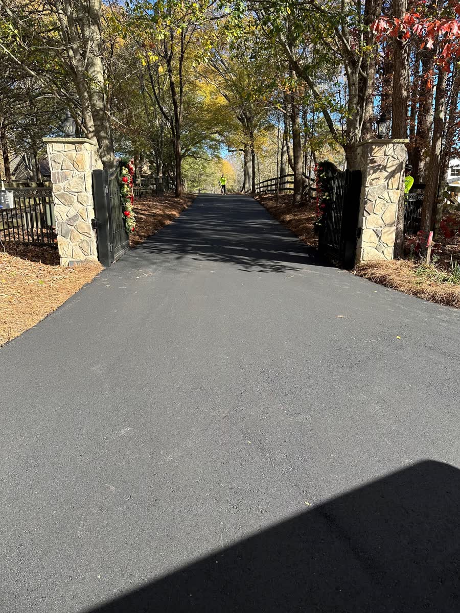 Long asphalt driveway winding between stone pillars and tall evergreen trees